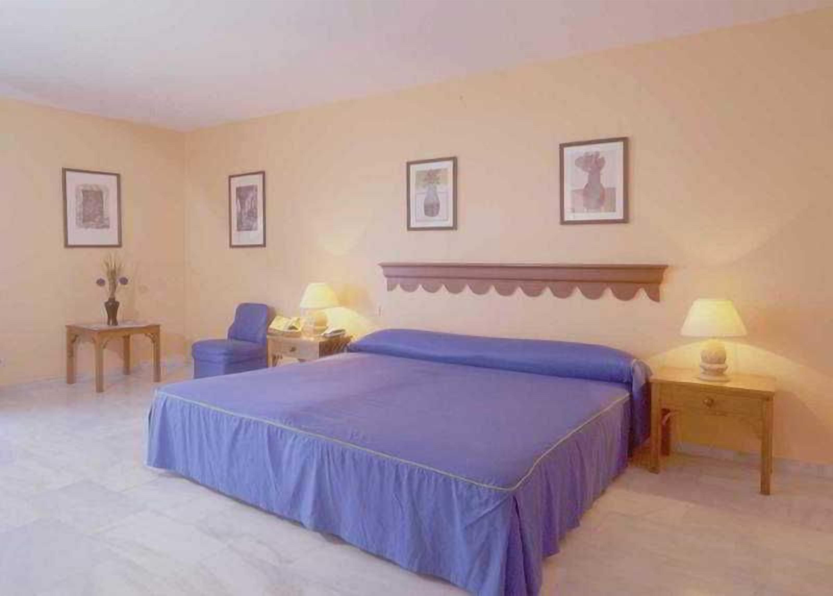 Een slaapkamer met een groot bed, twee nachtkastjes, een stoel en lijstjes met foto's aan de muur.