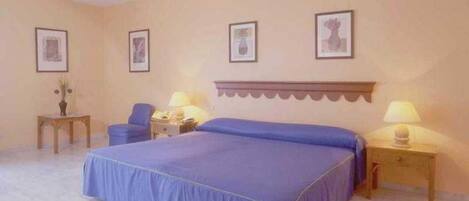 A bedroom with a large bed, two bedside tables, a chair, and framed pictures on the wall.