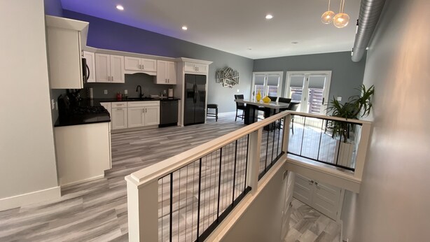A modern kitchen with white cabinets, a stainless steel refrigerator, and a dining area with a table and chairs. - The Flatts at North Shore (Geneva)