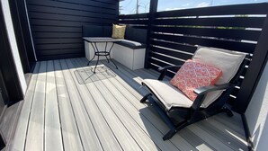 A covered outdoor deck with a table and chairs, a bench, and a view of the sky. - The Flatts at North Shore (Geneva)
