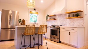 A modern kitchen with a central island, stainless steel appliances, and a hanging light fixture. - Pecan Paradise: near Beach & Downtown! (Wilmington)