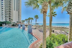 A swimming pool with a tiled deck, palm trees, and a view of the beach and ocean.