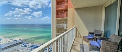 Ein Balkon mit Korbmöbeln mit Blick auf Strand und Meer.