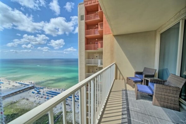 A balcony with wicker furniture overlooking a beach and ocean.