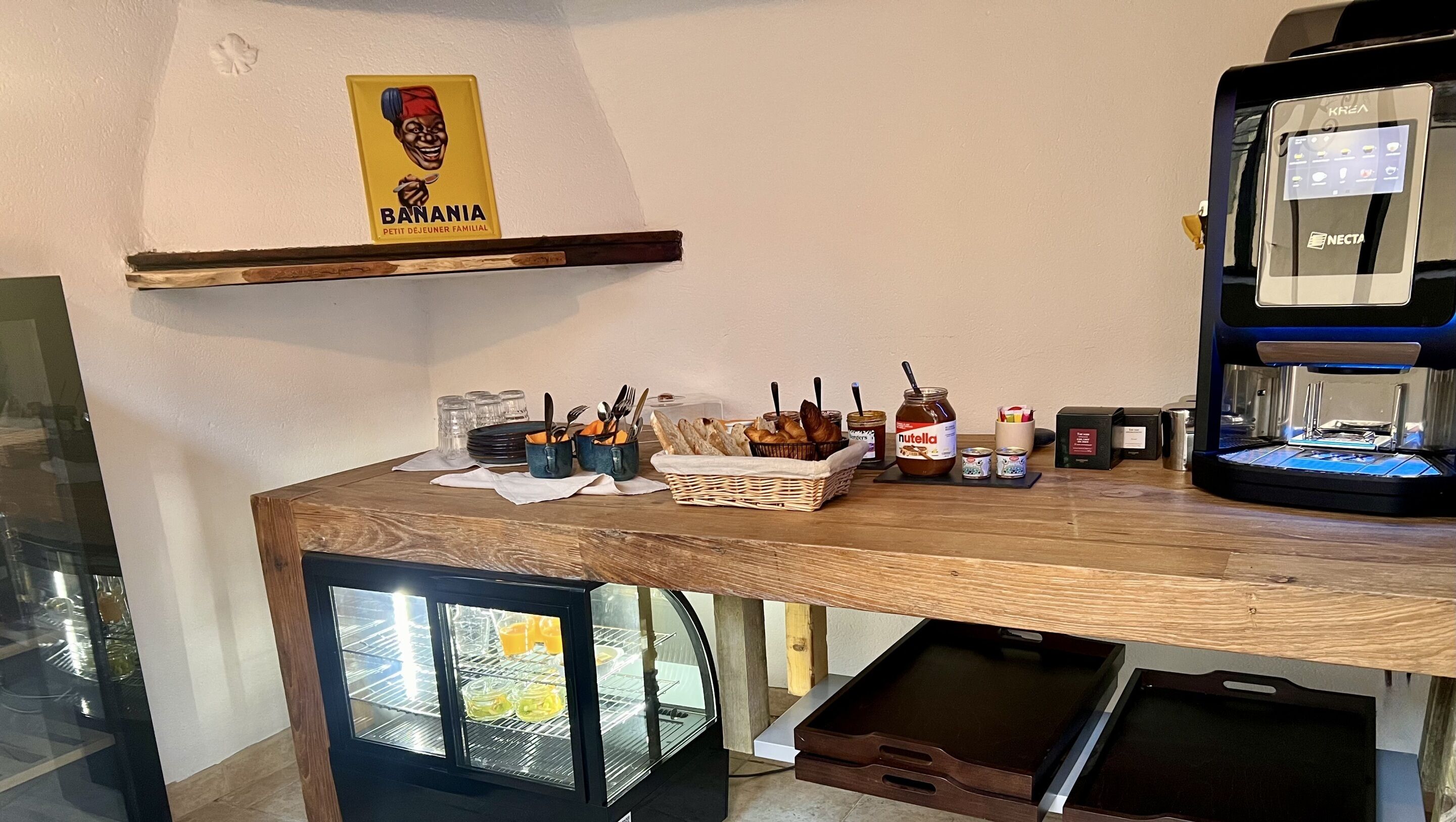 A kitchen area with a wooden table, a coffee machine, a refrigerator, and a sign above the counter.