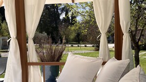 A cozy outdoor seating area with a wooden pergola, white cushions, and a striped towel. - Mas D'auseu (Plan-d'Orgon)