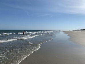 A beach with waves, a person in the water, and a distant shoreline. - Freshly Updated Villa Golf Course View Hilton Head (Hilton Head Island)