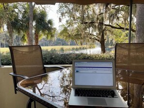 A laptop on a glass table with a view of a lake and trees. - Freshly Updated Villa Golf Course View Hilton Head (Hilton Head Island)