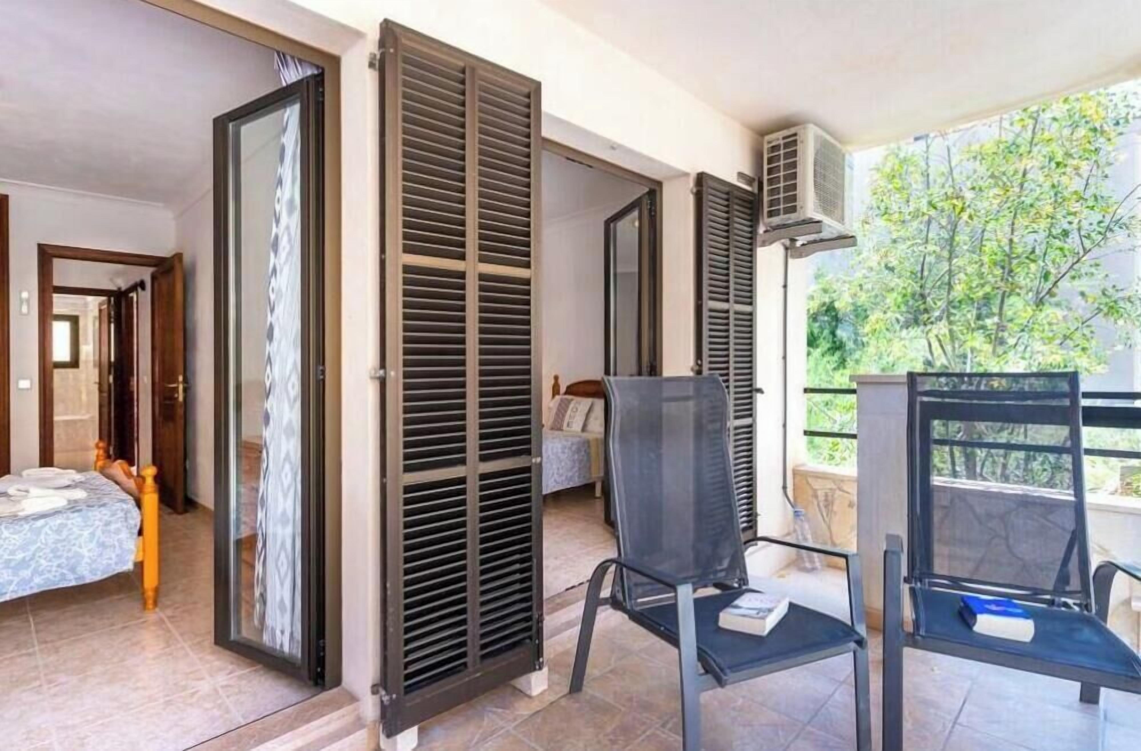 A room with a bed, a chair, and a balcony with a view of trees.