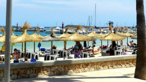 A beachside area with thatched umbrellas and lounge chairs, a stone wall, and a view of boats and a lighthouse in the background. - M0 Large apartment of 100 m2 + terraces (Sant Jordi)