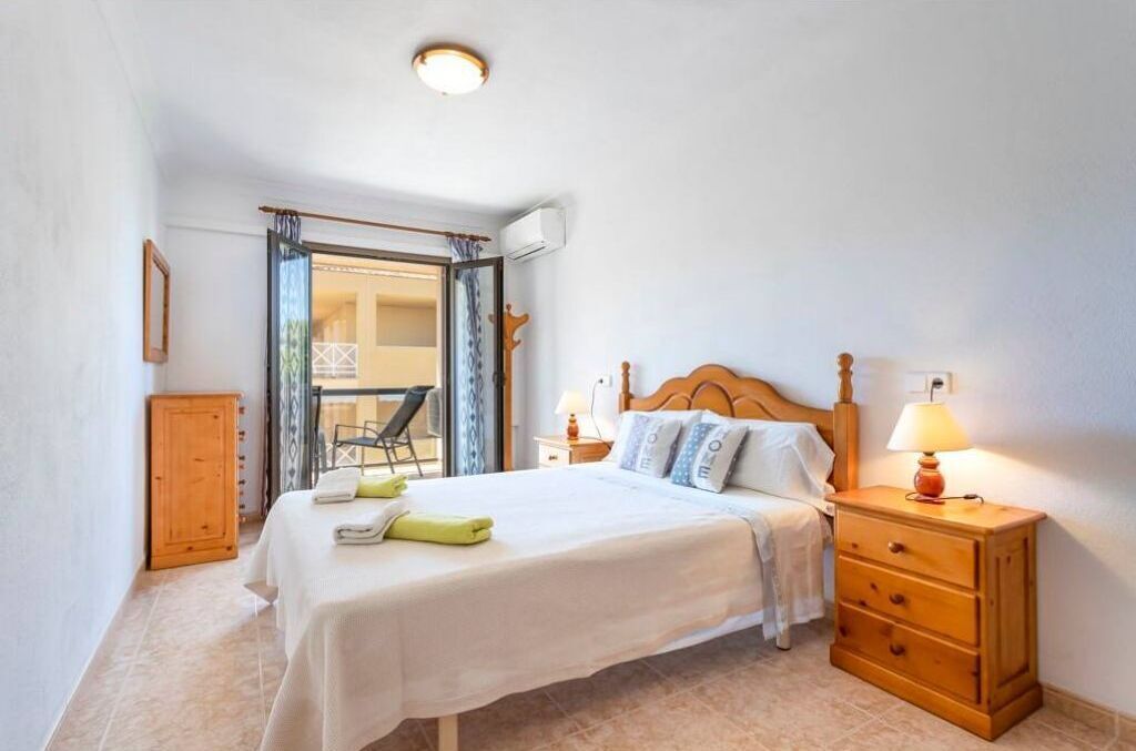 Un dormitorio con cama, mesitas de noche, un armario de madera y una ventana con cortinas.