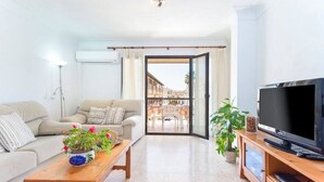 Een woonkamer met een bank, salontafel, televisie en uitzicht op een balkon.