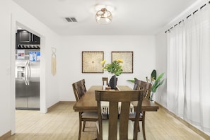 Un comedor moderno con una mesa y sillas de madera, un refrigerador y decoración en la pared.