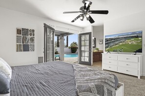Un dormitorio con una cama grande, ventilador de techo, televisor y vistas a una piscina y zona exterior.