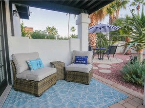 Dos sillones de mimbre con cojines y almohadas, un tapete estampado en azul y una sombrilla de patio.