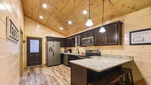 Una cocina moderna con paredes de madera, un refrigerador de acero inoxidable, un microondas y una encimera de granito.