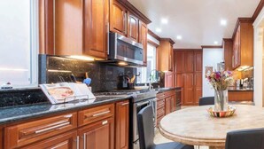 A modern kitchen with wooden cabinets, stainless steel appliances, and a round dining table with chairs. - Golden Gate Park 4BR Home | Garage + Metro Access (San Francisco)