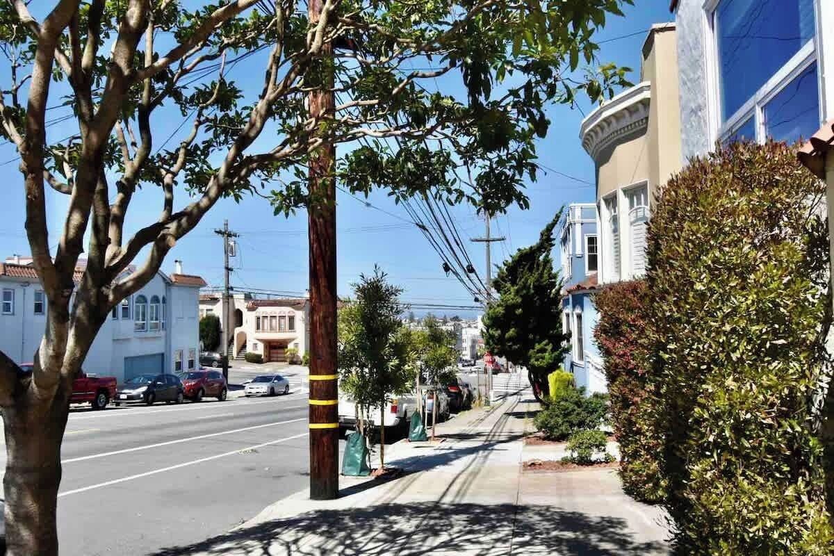 A street view with a sidewalk, parked cars, and buildings.