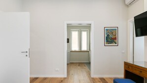 A room with a wooden floor, a white door, a desk with drawers, a blue bench, and a painting on the wall. - GuestHost - Elegant Don Giovanni flat of 60 sqm, for 4 people, located on the 5th floor of a historic building in Via Principe di Belmonte: NotHotel, a luxury Guest House, equipped with every comfort. Once inside you will be greeted by an elegant environ (Palermo)
