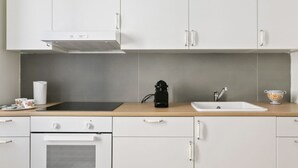 A modern kitchen with white cabinets, a black stove, a sink, and a coffee maker. - GuestHost - Elegant Don Giovanni flat of 60 sqm, for 4 people, located on the 5th floor of a historic building in Via Principe di Belmonte: NotHotel, a luxury Guest House, equipped with every comfort. Once inside you will be greeted by an elegant environ (Palermo)