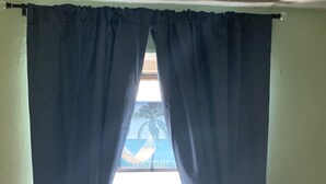 Ein Fenster mit dunklen Vorhängen und Blick aufs Meer, darunter eine Klimaanlage.