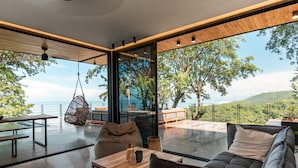 Un intérieur moderne avec une grande baie vitrée, un fauteuil suspendu, un canapé et une table en bois.