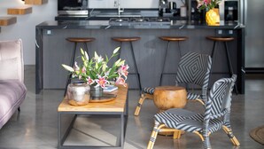 Une cuisine moderne dotée d’un îlot central, de tabourets de bar et d’un coin repas avec une chaise à motifs et une table agrémentée d’un vase de fleurs.