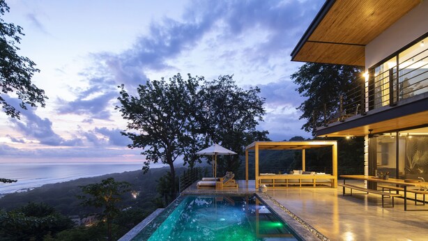 Un espace piscine extérieur moderne avec vue sur l’océan, entouré d’une végétation luxuriante et doté d’une terrasse en bois.