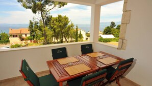 A dining area with a table and chairs, a view of the sea and buildings, and a balcony with a railing. - Villa Anni - Two-Bedroom Apartment with Terrace (Sutivan)