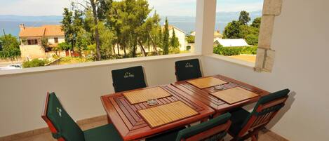 A dining area with a table and chairs, a view of the sea and buildings, and a balcony with a railing.