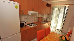 A compact kitchen with a refrigerator, stove, microwave, and sink. There is a dining table with orange chairs and a vase of flowers. - Villa Anni - Two-Bedroom Apartment with Terrace (Sutivan)