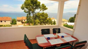 A balcony with a table and chairs, overlooking a coastal view with houses and trees. - Villa Anni-Two Bedroom Apartment with Sea View Terrace (Sutivan)