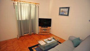A living room with a sofa, a glass coffee table, a flat-screen TV on a wooden stand, a door with a checkered curtain, and a framed picture on the wall. - Villa Anni-Two Bedroom Apartment with Sea View Terrace (Sutivan)