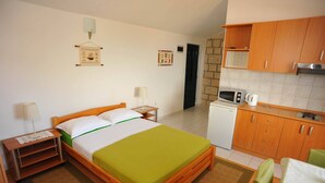 Ein Schlafzimmer mit Bett, Nachttisch, Lampe und einer kleinen Küchenzeile mit Mikrowelle und Wasserkocher.