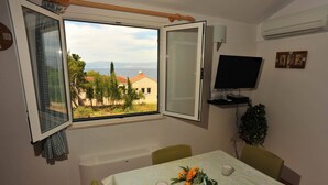 Ein Zimmer mit Tisch für zwei Personen, einem Fernseher und einem Fenster mit Blick auf Häuser und Bäume.