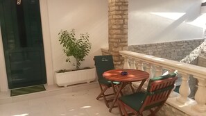 A balcony with a wooden table and chairs, a potted plant, and a stone wall.