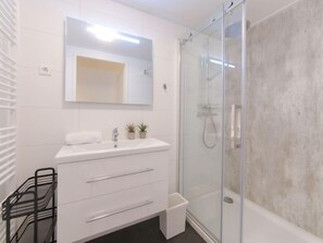 Un baño moderno con tocador blanco, cabina de ducha de vidrio y una pequeña planta en el lavabo.
