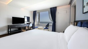 A hotel room with a large bed, a desk with a flat-screen TV, a chair, a small table, and a window with curtains. - Hotel HYGGELIG - Hostel (Busan)