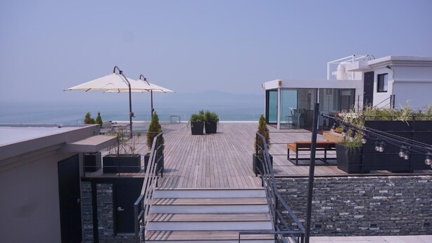 A rooftop terrace with a wooden deck, outdoor seating, and a view of the sea. - Hotel HYGGELIG - Hostel (Busan)