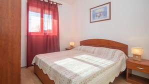 A bedroom with a wooden bed, a red curtain, a framed picture on the wall, and two bedside lamps. - Apartment Iva by Interhome (Pula/Krnica)