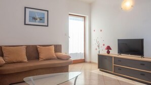 A living room with a sofa, a glass coffee table, a TV on a wooden cabinet, and a wall-mounted light fixture. - Apartment Iva by Interhome (Pula/Krnica)