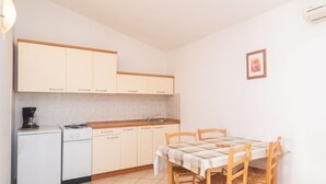 A compact kitchen with white cabinets, a small stove, and a dining table with chairs. - Apartment Iva by Interhome (Pula/Krnica)