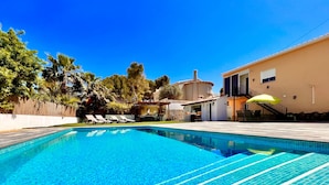 Ein Swimmingpool mit klarem, blauem Wasser, umgeben von Liegestühlen und einem Gebäude mit einem Balkon.