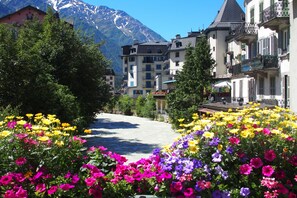 Un hôtel situé au pied d’une montagne, avec une rivière en premier plan et de magnifiques parterres de fleurs aux couleurs vives.