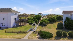 A residential area with houses, a wooden deck, and a pathway leading to a gazebo. - 1509 - Sandpiper - OBX Corolla Beach House w/ Pool & Hot Tub (Corolla)