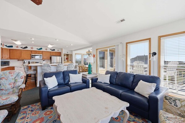 Ein modernes Wohnzimmer mit einem blauen Sofa, einem Esstisch und einer Küchenzeile mit Holzschränken und einer Mikrowelle.