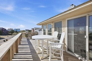 Une terrasse en bois avec une table et des chaises, une porte vitrée et une vue sur les maisons au loin.