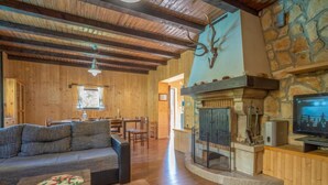 Interior acogedor de una cabaña con chimenea de piedra, vigas de madera en el techo y un televisor.