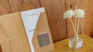 A wooden table with a cardholder, a card, and a perfume bottle. - Bed Station Hostel (Quy Nhon)