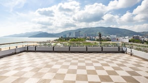 A spacious balcony with a checkered floor, overlooking a coastal cityscape with mountains in the background. - Bed Station Hostel (Quy Nhon)